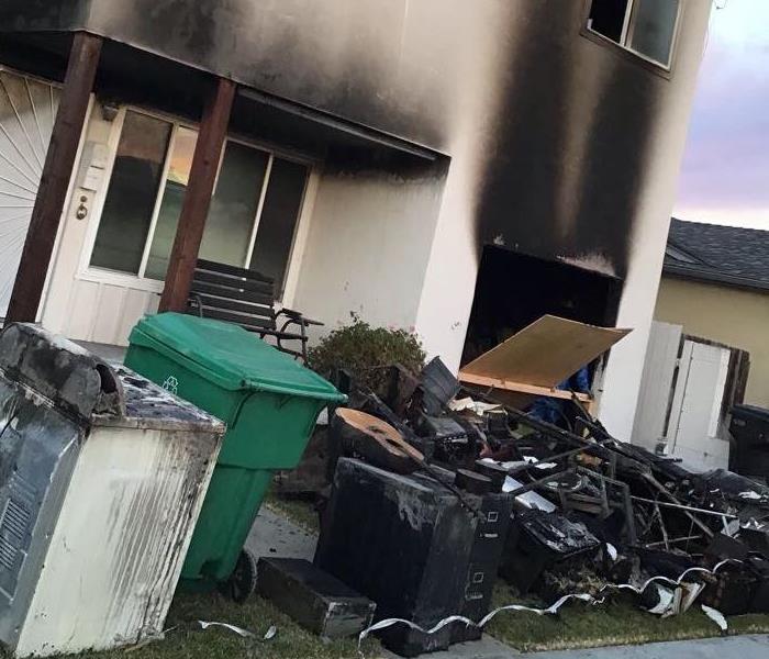 An unsecured building with heavy smoke damage and fire damaged items on the lawn.