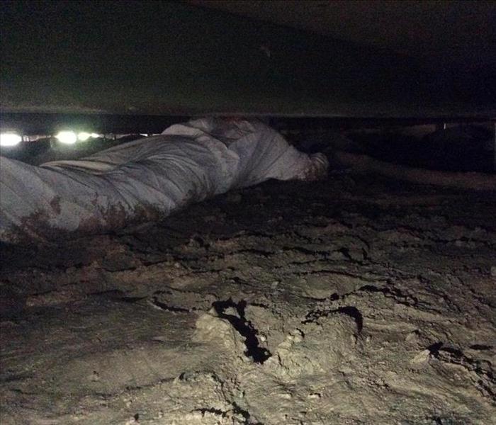 muddy crawlspace and person crawling in ppe suit with extraction hose