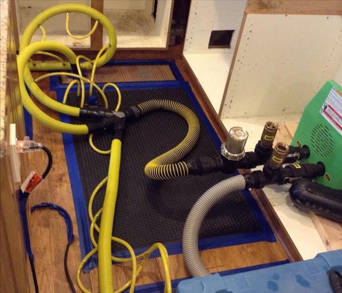 dehumidifier connected with hoses to floor drying mat on hardwood floors
